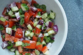 Light brown bowl filled with chopped cucumber, tomatoes, red onions, herbs and dressed with indian spices