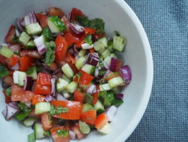 Light brown bowl filled with chopped cucumber, tomatoes, red onions, herbs and dressed with indian spices