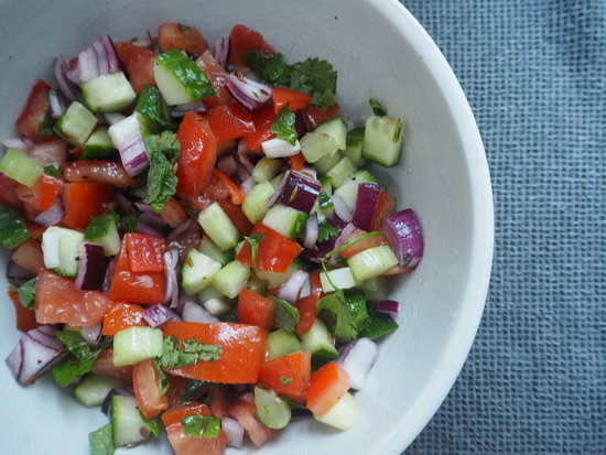 Light brown bowl filled with chopped cucumber, tomatoes, red onions, herbs and dressed with indian spices