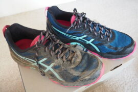 Pair of ASICS trainers on a shoe box, one dirty covered in mud the other brand new, box fresh
