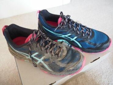 Pair of ASICS trainers on a shoe box, one dirty covered in mud the other brand new, box fresh