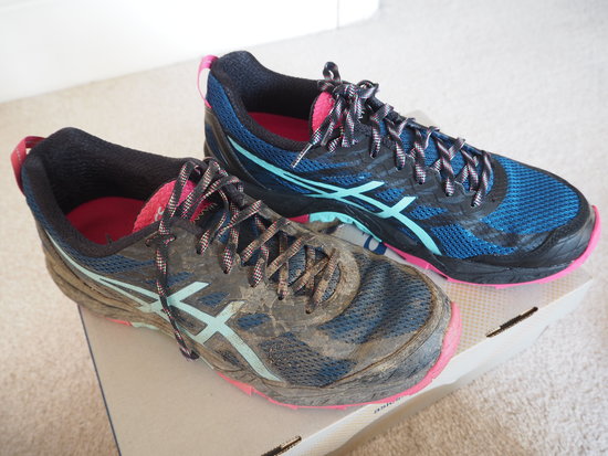Pair of ASICS trainers on a shoe box, one dirty covered in mud the other brand new, box fresh