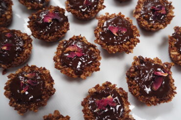 lots of small brown flapjacks covered in chocolate and decorated with rose petals