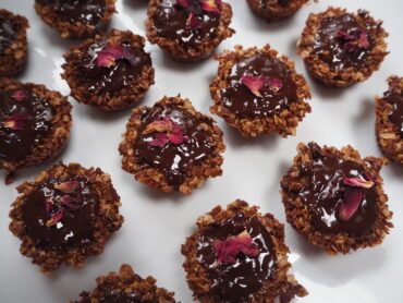 lots of small brown flapjacks covered in chocolate and decorated with rose petals