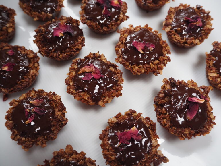 lots of small brown flapjacks covered in chocolate and decorated with rose petals