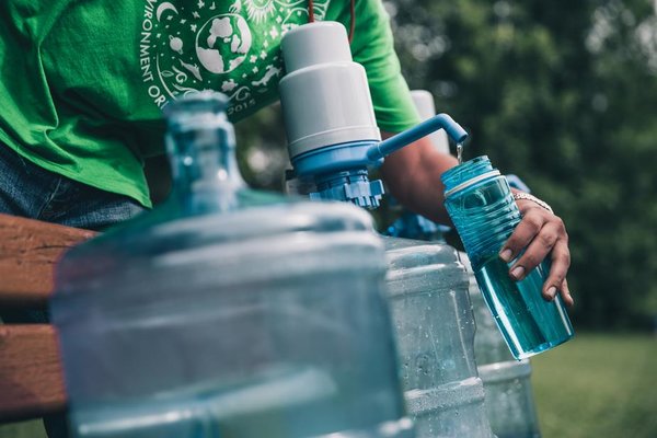 Close up picture of a person filling up a water bottle from a large clear cannister
