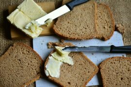 6 slices of brown bread on a chopping board wit two knives spreading lots of butter