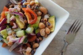 small square bowl filled with mixed bean salad on a wooden worktop with fork