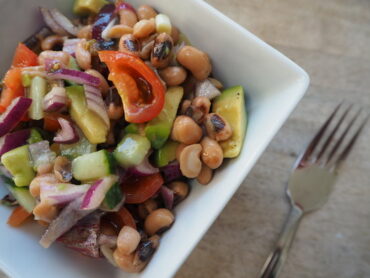small square bowl filled with mixed bean salad on a wooden worktop with fork