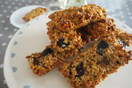 Pile of rectangular flapjacks with figs and walnuts in them sat on a cream cake stand