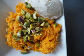 Close up of this carrot based dessert sprinkled with chopped pistachio nuts and a scoop of white vanilla ice cream in the top right hand corner