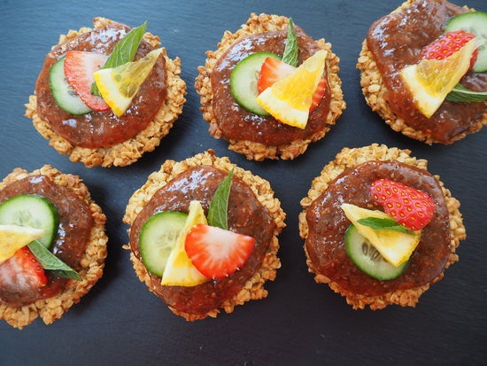 6 round flapjacks topped with Pimms strawberry jam and decorated with sliced strawberry, lemon, cucumber and mint leaf, on a dark grey slate background
