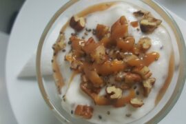 Close up of top of small glass bowl filled with white dessert and topped with stacked pecans nuts and caramel drizzle