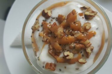 Close up of top of small glass bowl filled with white dessert and topped with stacked pecans nuts and caramel drizzle