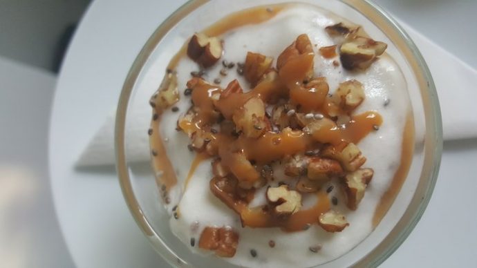 Close up of top of small glass bowl filled with white dessert and topped with stacked pecans nuts and caramel drizzle