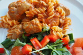 Close up of pasta twirls in tomato sauce with sausage meatballs and a side salad