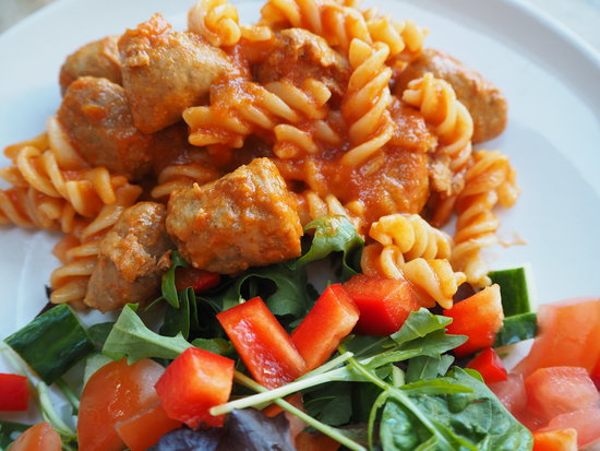 Close up of pasta twirls in tomato sauce with sausage meatballs and a side salad