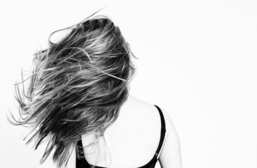 Black and white image of the back of a femaile with long hair being flicked out to the side.
