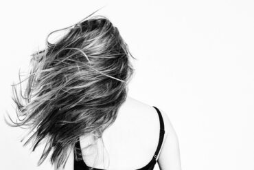 Black and white image of the back of a femaile with long hair being flicked out to the side.