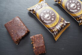3 Pulsin Salted Caramel Raw Choc Brownies - 1 unwrapped an broken into 2/3 and 1/3, 2 in the wrapper on a dark slate background