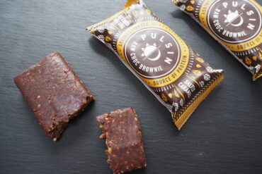 3 Pulsin Salted Caramel Raw Choc Brownies - 1 unwrapped an broken into 2/3 and 1/3, 2 in the wrapper on a dark slate background