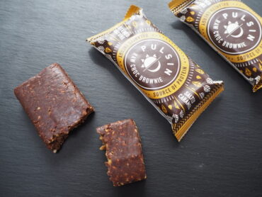 3 Pulsin Salted Caramel Raw Choc Brownies - 1 unwrapped an broken into 2/3 and 1/3, 2 in the wrapper on a dark slate background