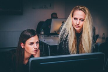 two female office workers looking at a computer screen and experiencing eye strain