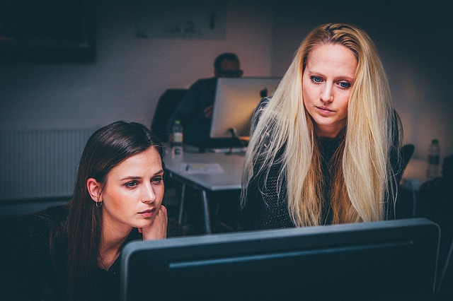 two female office workers looking at a computer screen and experiencing eye strain