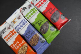 four packets of Munchy Seeds positioned diagonally on a dark slate background.