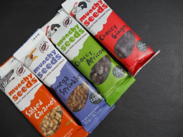 four packets of Munchy Seeds positioned diagonally on a dark slate background.