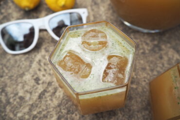 2 lemons, white sunglasses close up of top of glass filled with mint lemonade and 3 ice cubes