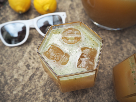 2 lemons, white sunglasses close up of top of glass filled with mint lemonade and 3 ice cubes