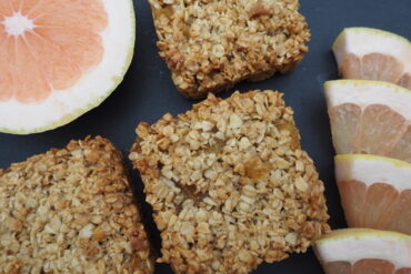 Close up of three pineapple and grapefruit flapjacks with half a grapefruit and 4 slices of grapefruit to the side