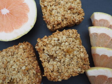 Close up of three pineapple and grapefruit flapjacks with half a grapefruit and 4 slices of grapefruit to the side