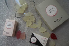 Vinoos real wine gums scattered with packaging and wine glass. They are shaped like little bunches of grapes and come in red, rose and white wine flavours