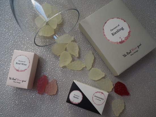 Vinoos real wine gums scattered with packaging and wine glass. They are shaped like little bunches of grapes and come in red, rose and white wine flavours