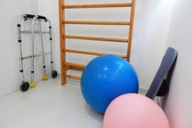 White room containing physical therapy equipment including a blue and pink exercise balls and walking frames