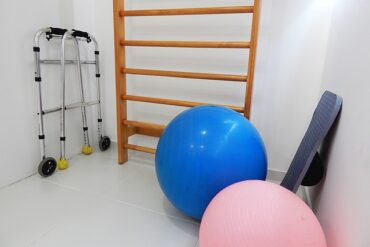 White room containing physical therapy equipment including a blue and pink exercise balls and walking frames