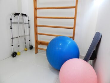 White room containing physical therapy equipment including a blue and pink exercise balls and walking frames