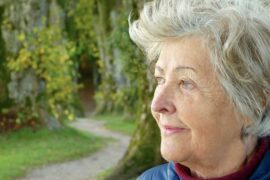Old lady staring into the distance in outdoor park looking as if she has dementia