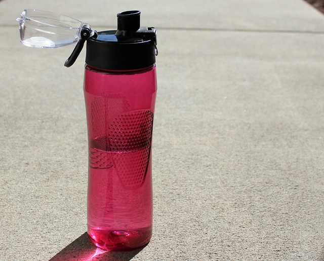 Half full red water bottle on a pavement to indicate hydrating well to prevent chafing
