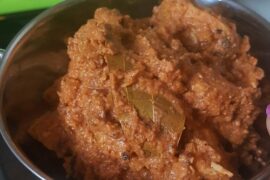 Close up of Makhani Murgh also known as Butter Chicken in a silver bowl in front of a close up of TV screen showing a football pitch