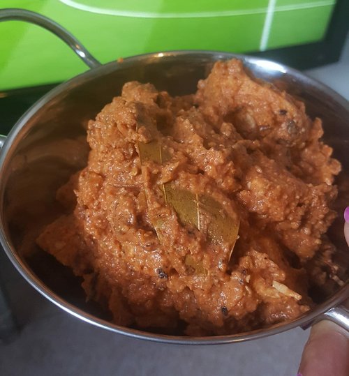 Close up of Makhani Murgh also known as Butter Chicken in a silver bowl in front of a close up of TV screen showing a football pitch