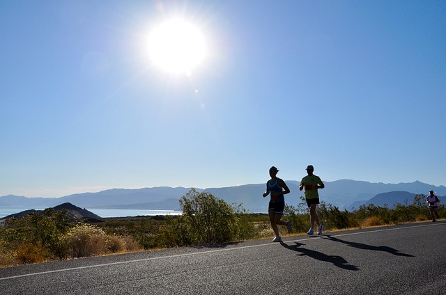 two people running on a road alongside a beach on a hot day. they're wearing shorts and likely to be suffering from thigh chafing in the hot weather.