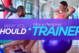 Male personal trainer assisting a female doing sit ups sat on a blue exercise ball