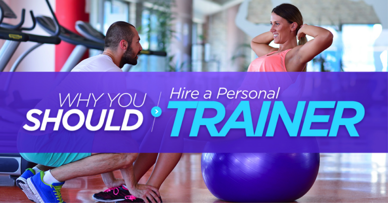 Male personal trainer assisting a female doing sit ups sat on a blue exercise ball