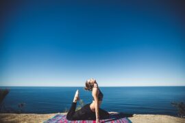 Female in lycra practising yoga on a cliffside overlooking the ocean and beautiful clear blue sky