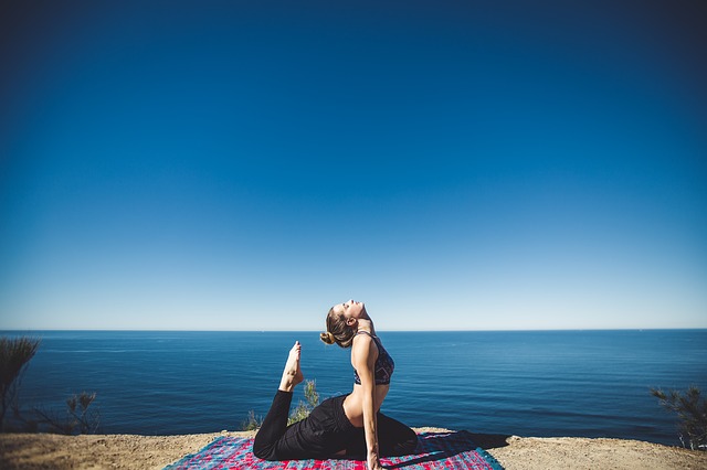Female in lycra practising yoga on a cliffside overlooking the ocean and beautiful clear blue sky