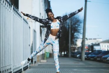 Young black female doing half a star jump, wearing sports gear and happy she's found the right workout plan