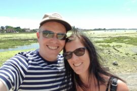 Headshot of male and female wearing sunglasses smiling with beautiful natural harbour in the background. The picture of a healthy happy relationship